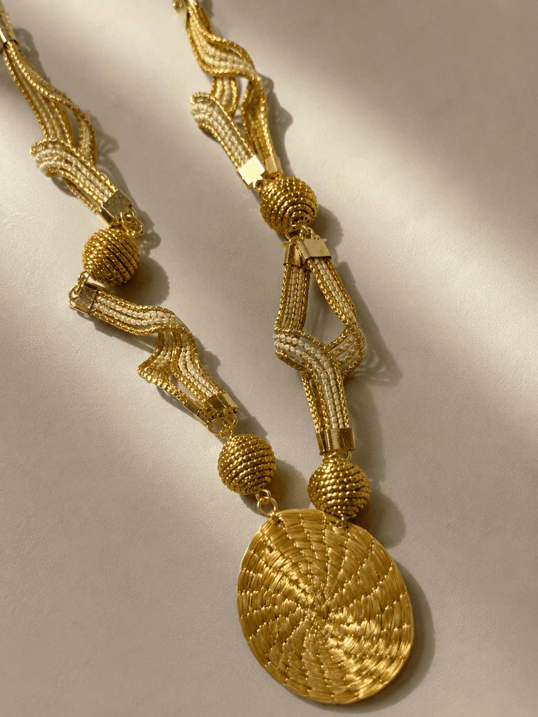 Colar Solaris dourado com detalhes claros, esferas artesanais e grande medalhão central