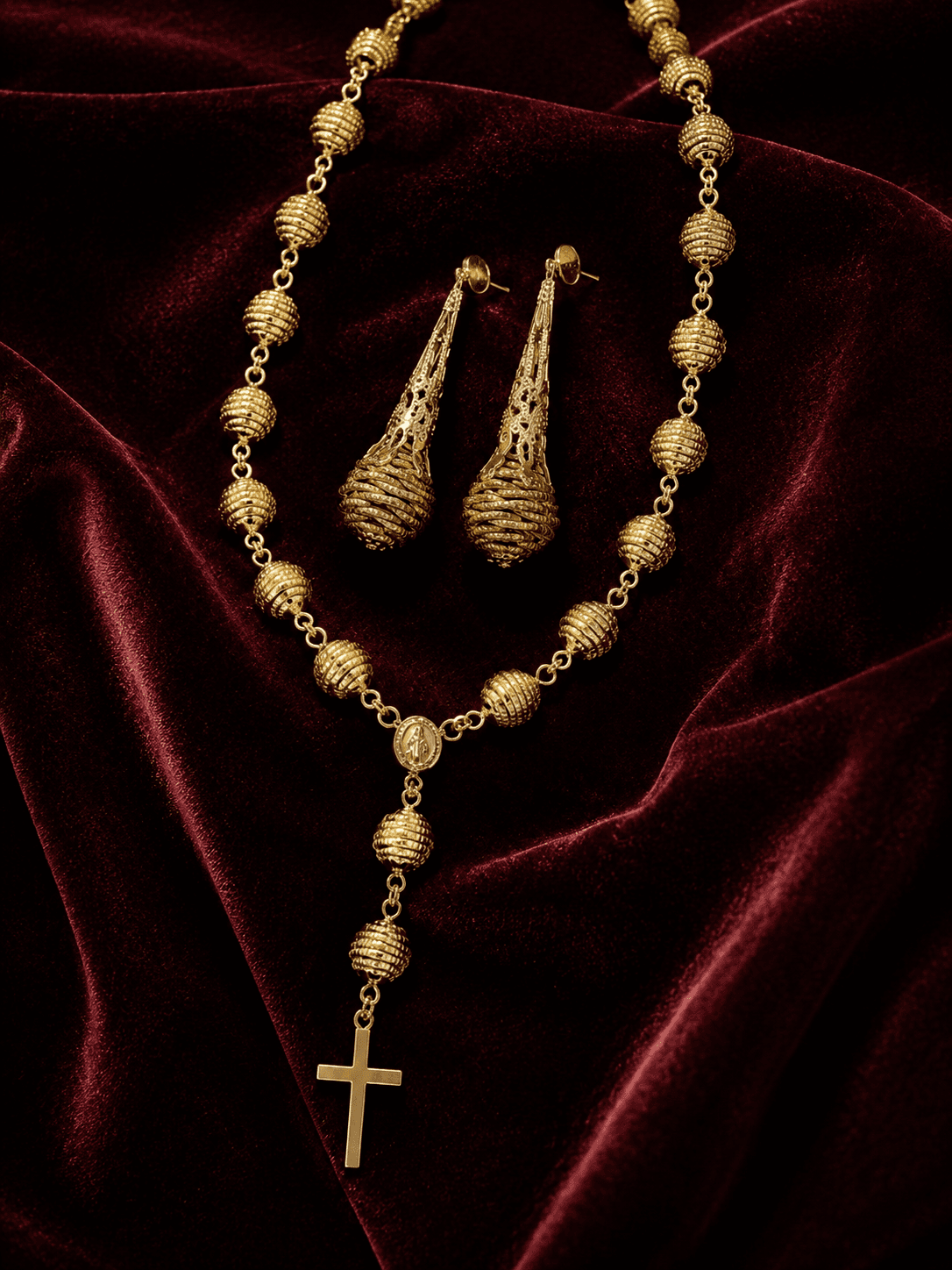 Conjunto Origem com terço e par de brincos dourados artesanais sobre veludo vermelho